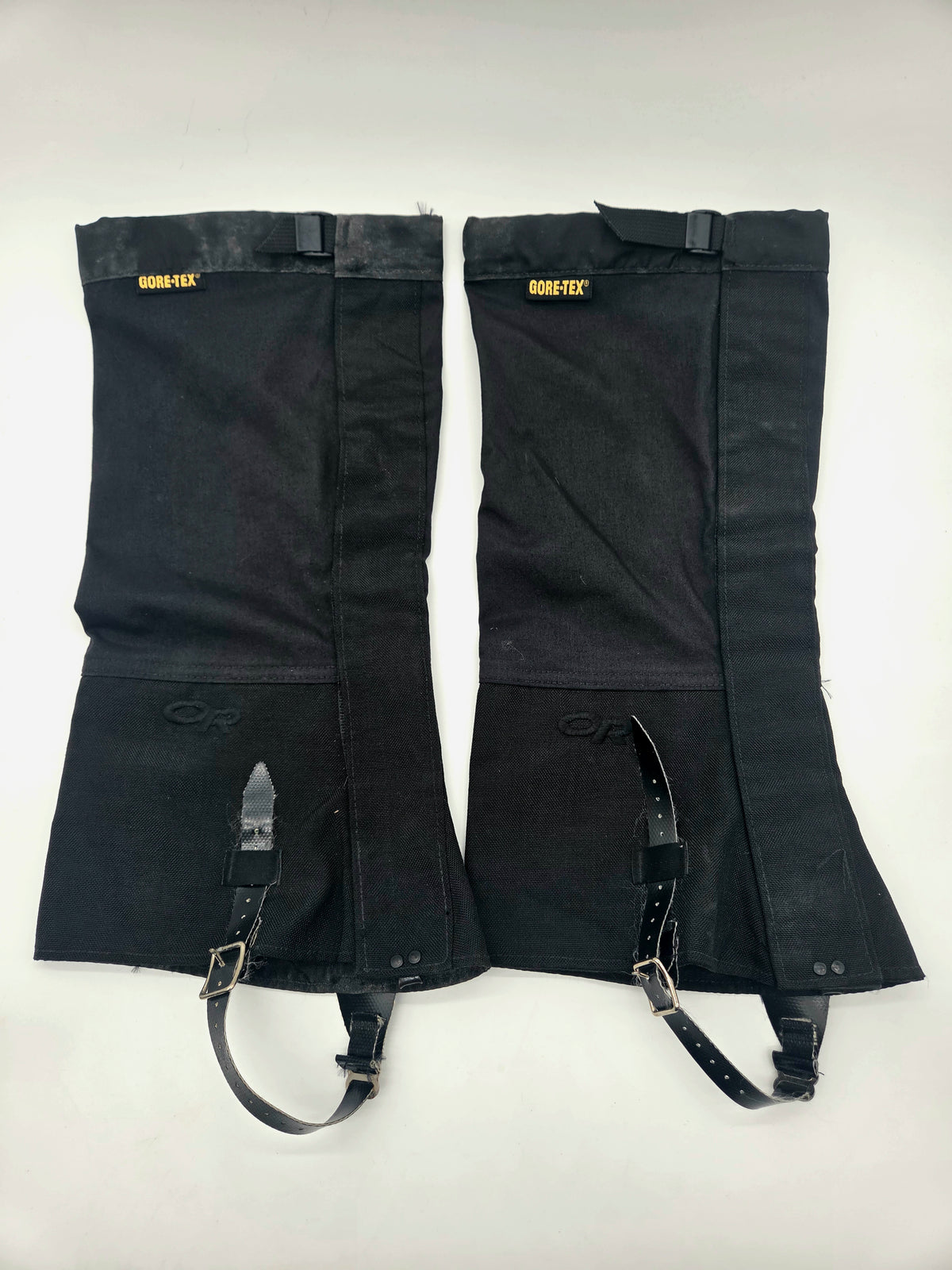 A pair of black GORE-TEX insulated gaiters with adjustable black straps and metal buckles, laid flat on a white background.